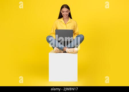 Lady Working On Laptop Computer Smiling Sitting Over Yellow Background Stock Photo