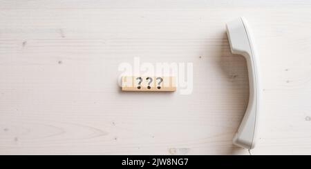 Three question marks written on wooden peg placed next to a white landline telephone receiver in a conceptual image of customer help and support. Over Stock Photo