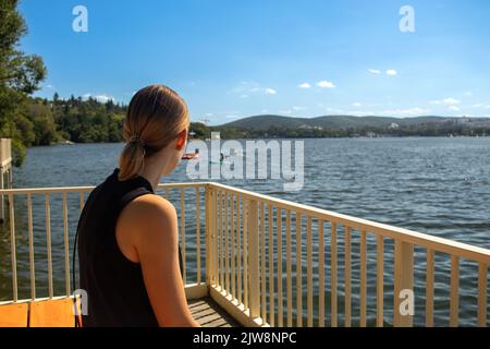 Beauty of a young woman from behind sitting on a pier waiting for a ship. Stock Photo