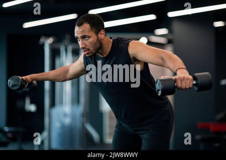 Muscular Black Young Man Doing Dumbbell Lateral Raise Exercise At Gym Stock Photo