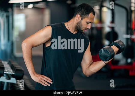 Handsome young african american man doing bodybuilding workout with dumbbell at gym Stock Photo