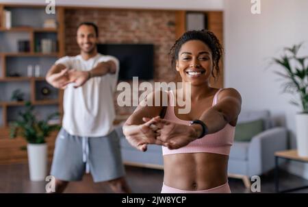 Happy young african american man and woman in sportswear doing stretching or warm up exercises Stock Photo