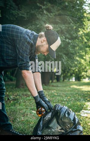 A young man with a trash bag in the forest cleans up plastic bottles. Stock Photo