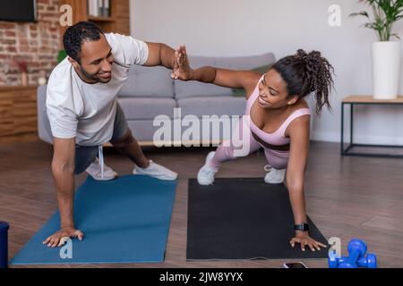 Smiling young african american lady and guy in sportswear doing plank exercises and give high five Stock Photo
