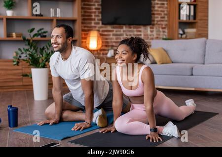 Satisfied young african american guy and lady in sportswear doing leg stretching and practicing yoga Stock Photo