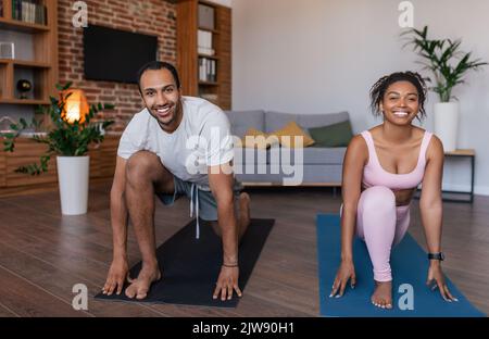Smiling young black man and lady in sportswear doing leg exercises, stretching or practicing yoga together Stock Photo