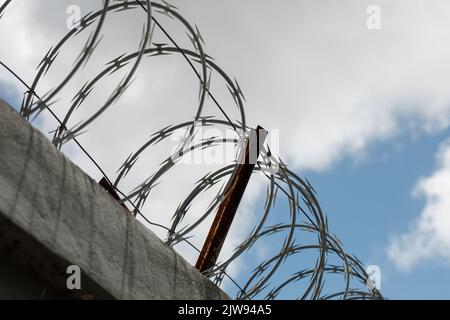 Chain link fence with barbed wire and razor wire. against the blue sky. Stock Photo