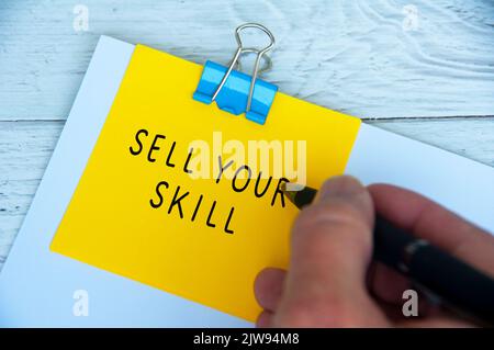 Hand writing sell your skill text on yellow notepad. Skill concept. Stock Photo