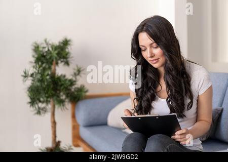 Portrait of a young woman in the office. Woman writes data to the questionnaire. Stock Photo