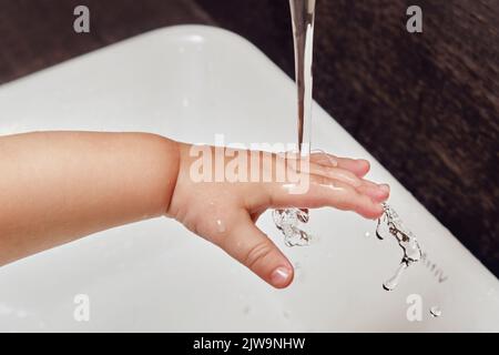 Toddler baby hand is washed under running water from the tap in the sink. Child learns to wash his hands Stock Photo