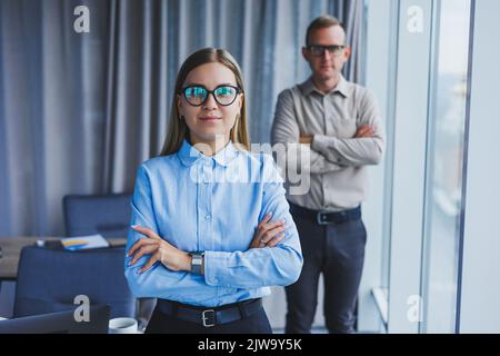 Several friendly colleagues are standing by the office window. A business woman in glasses stands on the background of a man in a shirt. Selective foc Stock Photo