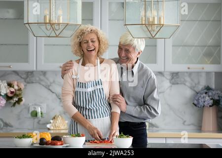 Cheerful mature couple cooking healthy meal for dinner together Stock Photo