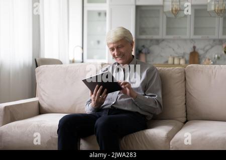 Happy senior tablet user using digital device on home couch Stock Photo