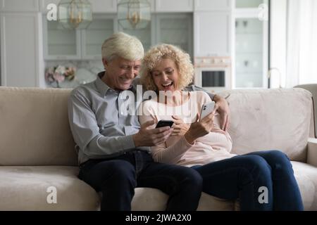 Happy cheerful retired couple using online apps on smartphones Stock Photo