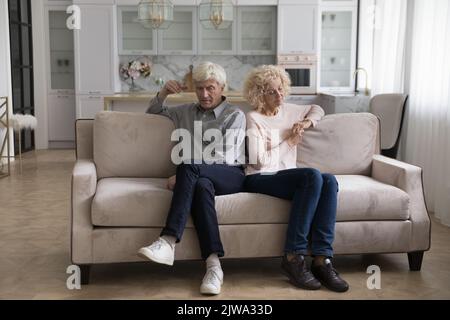Angry stressed senior couple sitting on couch with back touches Stock Photo