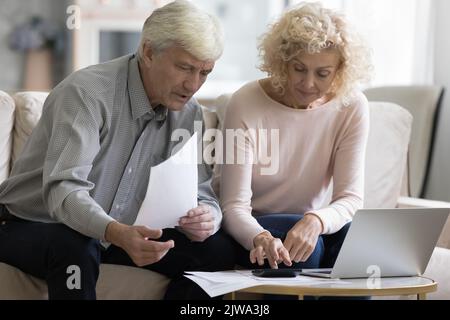 Focused retired married couple checking paper bills, invoices Stock Photo