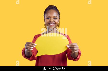 Paper blank mockup of speech bubble in hands of smiling african american woman on yellow background. Stock Photo