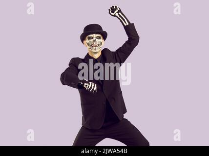 Cheerful man with skeleton makeup on his face having fun dancing at Halloween costume party.