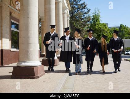 Group of graduates talk as they walk around college campus after awards ceremony. Stock Photo