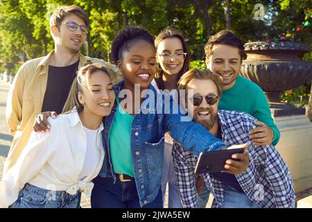 Multiethnic young happy people take collective selfie with friends on phone stands on city street Stock Photo
