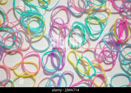 background set of small multi-colored rubber bands on a white sunny table. Stock Photo