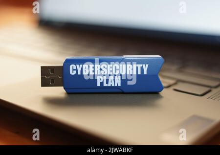 On the laptop keyboard is a flash drive with the inscription - Cybersecurity Plan Stock Photo