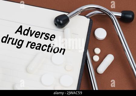 On a brown surface lies a stethoscope, pills and a notepad with the inscription - adverse drug reaction Stock Photo
