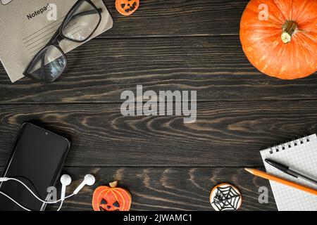 Halloween lifestyle background, top view. Pumpkin, sweets and accessories on dark wooden table, flat lay. Frame of Halloween food, glasses, phone on w Stock Photo