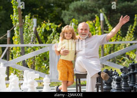 Grandfather and young child grandson playing chess on big chess board. Spending time together with granddad. Stock Photo