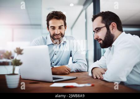 Putting their heads together to get tasks done quicker. two businessmen working together on a laptop in an office. Stock Photo