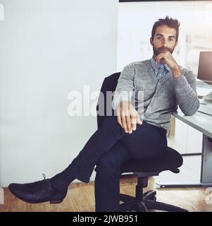 Hes got a confident demeanour. Cropped portrait of a handsome young businessman looking thoughtful while sitting in the office. Stock Photo