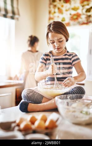 Shes a busy little baker. a little girl baking with her mother in the kitchen. Stock Photo