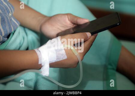 Female patient after giving baby birth, checking touchscreen phone with iv line on hand in the hospital. Stock Photo