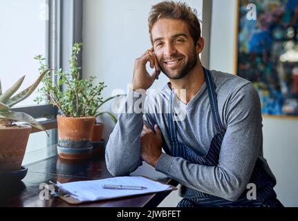 Barista and business owner combined. a handsome young barista using a mobile phone while working in his coffee shop. Stock Photo