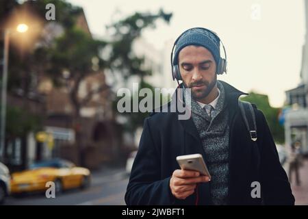 Music is my escape. a fashionable young man listening to music on his phone while out in the city. Stock Photo