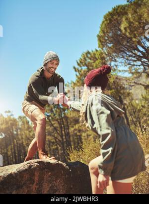 Hes always there to help her up. a man giving his girlfriend a hand while out hiking. Stock Photo