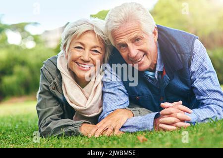 Feels good to get out. Portrait of a happy senior couple lying down on the grass together in the park. Stock Photo