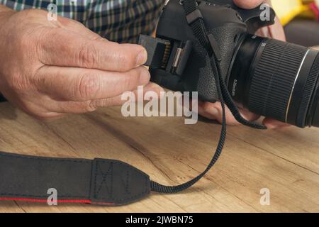 Male photographer inserting a flash memory card while holding a professional camera. Stock Photo