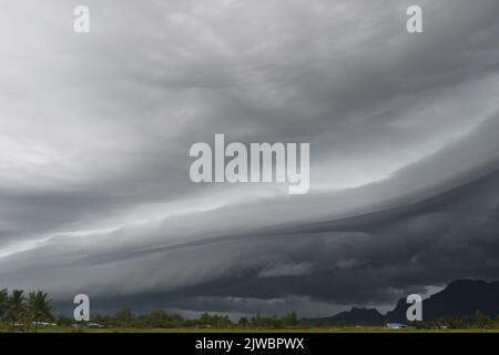 Gray Cumulonimbus cloud formations on sky above mountain, Nimbus moving with rice field,  Arcus cloud rolling in the storm with Appearance of rain clo Stock Photo