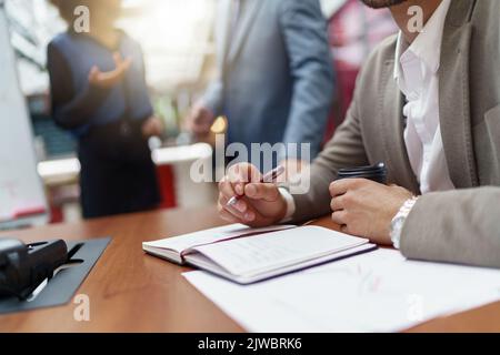 Close up of businessman making notes sitting in office on colleagues background Stock Photo