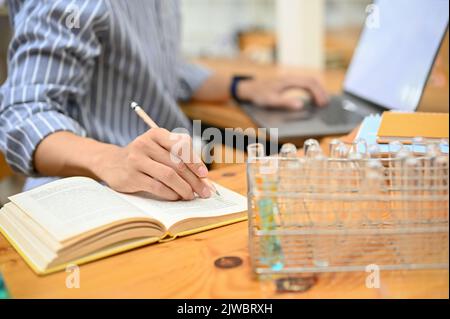 Close-up shot, A professional male scientist or chemist working on his science experiment research at his office, using laptop and taking notes on his Stock Photo