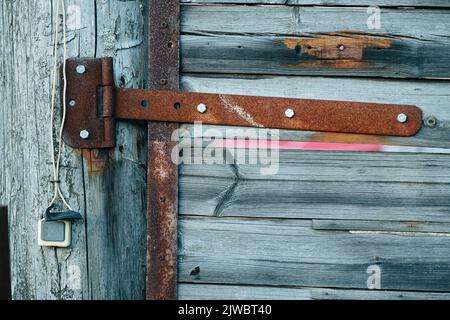 Rusted strap hinge on a fence gate door made from withered grey wood with shiny stainless bolt heads. Old buzzer at the side. Stock Photo