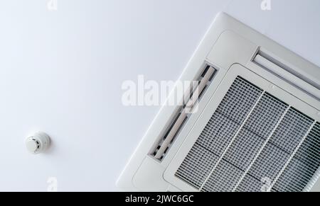 Cassette type air conditioner and smoke detector mounted on ceiling wall. Air duct on ceiling in hotel. Air heading unit on gypsum wall. Cool system i Stock Photo