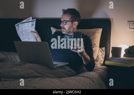 Man works with laptop lying on bed. Male home working with remote office. Boy sitting in bedroom use online devices. Smart working, home school, inter Stock Photo