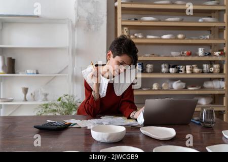 Focused young woman ceramic studio owner analyzing bills and receipts, doing pottery cost analysis Stock Photo