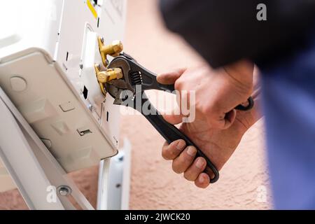 Close upof male worker's hands tightening wrench of air conditioner with wrench. HVAC technician is working on air conditioner units on wall of new in Stock Photo