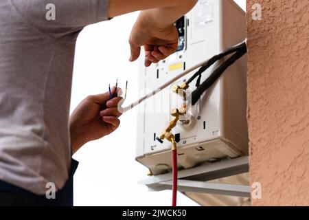 Male worker connects electrical wires during installation of air conditioner. Close up of man serving exterior of air conditioner unit hanging on wall Stock Photo