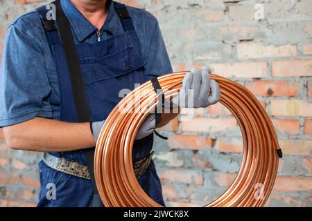 Heating system and underfloor heating. Heating red electrical cable in hands of male electrician technician dressed in overalls. Close up of building Stock Photo