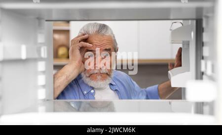 Portrait Of Hungry Elderly Man Searching For Food In Empty Fridge Stock Photo