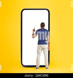 Black Man Using Phone Standing Back To Camera, Yellow Background Stock Photo